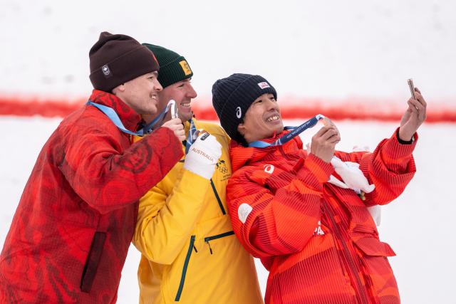 (260212) -- LIVIGNO, Feb. 12, 2026 (Xinhua) -- Gold medalist Cooper Woods (C) of Australia, silver medalist Mikael Kingsbury (L) of Canada and bronze medalist Horishima Ikuma of Japan take a selfie during the awarding ceremony of the freestyle skiing men's moguls match at the Milan-Cortina 2026 Olympic Winter Games in Livigno, Italy, Feb. 12, 2026. (Xinhua/Hu Chao)