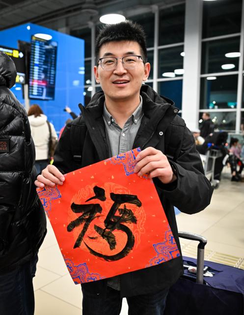 (260214) -- ALMATY, Feb. 14, 2026 (Xinhua) -- A Chinese passenger displays Chinese character "Fu" (meaning good fortune) during a Chinese New Year cultural event at the Almaty International Airport in Almaty, Kazakhstan, Feb. 13, 2026. (Xinhua/Li Renzi)