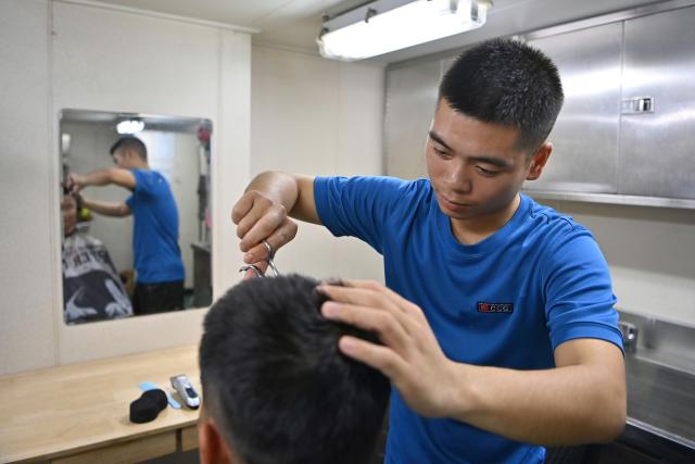 (260214) -- SOUTH CHINA SEA, Feb. 14, 2026 (Xinhua) -- Law enforcer Wang Hong cuts hair for one of his comrades aboard the China Coast Guard (CCG) vessel Wanshan in the territorial waters of China's Huangyan Dao, Feb. 11, 2026. Right ahead of the Chinese New Year, a traditional occasion for family reunion in China, a group of young law enforcers remain loyally stationed and highly alert around the clock, hundreds of miles away from their loved ones. (Photo by Zhai Yifan/Xinhua)