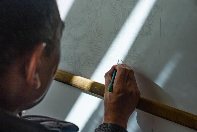 (260216) -- LHASA, Feb. 16, 2026 (Xinhua) -- Norbu Sidar draws the pattern of a thangka at his office at the Xizang Academy of Thangka in Lhasa, southwest China's Xizang Autonomous Region, Feb. 10, 2026. On the afternoon of Feb. 10, sunlight streamed through the windows of the Xizang Academy of Thangka, illuminating an unfinished thangka painting. Norbu Sidar stood beside a young apprentice. He reached out, gently placing his finger on a specific spot on the canvas, and quietly guided the apprentice on the direction of the lines. 
   Thangka, renowned for its meticulous composition, vibrant colors, and profound cultural connotations, was listed among the first batch of China's national intangible cultural heritages in 2006. Recording Tibetan history, culture, medicine, astronomy, and other knowledge, it carries the spiritual beliefs and aesthetic wisdom of people in Xizang throughout the times.
   Norbu Sidar is a national-level inheritor of the Tibetan thangka. As a child, he learned thangka painting techniques from his grandfather. He recalled, "Time was most precious when I was little. I could only learn to paint thangka in my spare time after helping the family with farm and livestock work." From 2005 to 2015, he spent ten years as a restoration expert undertaking the mural restoration project at the Potala Palace. In 2016, he donated the 18 thangka works he had copied at the Potala Palace over the decade to the Palace. "These ten years have been the most meaningful part of my life," he recalled.
   In 1992, Norbu Sidar began taking on students. Ten years later, he led the founding of the Xizang Academy of Thangka. Today, as a master's supervisor at the School of Arts of Xizang University, he guides graduate students in studying the history of thangka and encourages young people to experiment with new forms of expression. To date, over 400 students are, like him, contributing to the development of Tibetan thangka art.
    After being elected as a member of the National Committee of the Chinese People's Political Consultative Conference, Norbu Sidar felt he had the responsibility to do more to make thangka, the artistic treasure in Xizang, recognized, supported and passed down through generations. (Xinhua/Tenzin Nyida)
