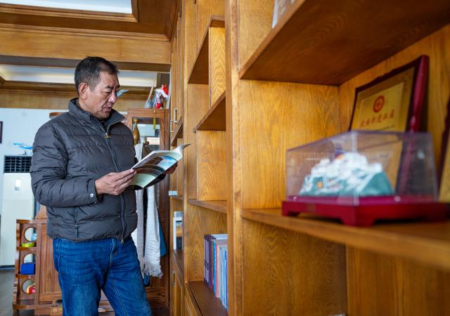 (260216) -- LHASA, Feb. 16, 2026 (Xinhua) -- Norbu Sidar reads books at his office at the Xizang Academy of Thangka in Lhasa, southwest China's Xizang Autonomous Region, Feb. 10, 2026. On the afternoon of Feb. 10, sunlight streamed through the windows of the Xizang Academy of Thangka, illuminating an unfinished thangka painting. Norbu Sidar stood beside a young apprentice. He reached out, gently placing his finger on a specific spot on the canvas, and quietly guided the apprentice on the direction of the lines. 
   Thangka, renowned for its meticulous composition, vibrant colors, and profound cultural connotations, was listed among the first batch of China's national intangible cultural heritages in 2006. Recording Tibetan history, culture, medicine, astronomy, and other knowledge, it carries the spiritual beliefs and aesthetic wisdom of people in Xizang throughout the times.
   Norbu Sidar is a national-level inheritor of the Tibetan thangka. As a child, he learned thangka painting techniques from his grandfather. He recalled, "Time was most precious when I was little. I could only learn to paint thangka in my spare time after helping the family with farm and livestock work." From 2005 to 2015, he spent ten years as a restoration expert undertaking the mural restoration project at the Potala Palace. In 2016, he donated the 18 thangka works he had copied at the Potala Palace over the decade to the Palace. "These ten years have been the most meaningful part of my life," he recalled.
   In 1992, Norbu Sidar began taking on students. Ten years later, he led the founding of the Xizang Academy of Thangka. Today, as a master's supervisor at the School of Arts of Xizang University, he guides graduate students in studying the history of thangka and encourages young people to experiment with new forms of expression. To date, over 400 students are, like him, contributing to the development of Tibetan thangka art.
    After being elected as a member of the National Committee of the Chinese People's Political Consultative Conference, Norbu Sidar felt he had the responsibility to do more to make thangka, the artistic treasure in Xizang, recognized, supported and passed down through generations. (Xinhua/Tenzin Nyida)