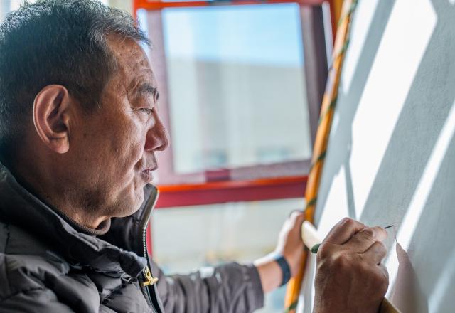 (260216) -- LHASA, Feb. 16, 2026 (Xinhua) -- Norbu Sidar draws the pattern of a thangka at his office at the Xizang Academy of Thangka in Lhasa, southwest China's Xizang Autonomous Region, Feb. 10, 2026. On the afternoon of Feb. 10, sunlight streamed through the windows of the Xizang Academy of Thangka, illuminating an unfinished thangka painting. Norbu Sidar stood beside a young apprentice. He reached out, gently placing his finger on a specific spot on the canvas, and quietly guided the apprentice on the direction of the lines. 
   Thangka, renowned for its meticulous composition, vibrant colors, and profound cultural connotations, was listed among the first batch of China's national intangible cultural heritages in 2006. Recording Tibetan history, culture, medicine, astronomy, and other knowledge, it carries the spiritual beliefs and aesthetic wisdom of people in Xizang throughout the times.
   Norbu Sidar is a national-level inheritor of the Tibetan thangka. As a child, he learned thangka painting techniques from his grandfather. He recalled, "Time was most precious when I was little. I could only learn to paint thangka in my spare time after helping the family with farm and livestock work." From 2005 to 2015, he spent ten years as a restoration expert undertaking the mural restoration project at the Potala Palace. In 2016, he donated the 18 thangka works he had copied at the Potala Palace over the decade to the Palace. "These ten years have been the most meaningful part of my life," he recalled.
   In 1992, Norbu Sidar began taking on students. Ten years later, he led the founding of the Xizang Academy of Thangka. Today, as a master's supervisor at the School of Arts of Xizang University, he guides graduate students in studying the history of thangka and encourages young people to experiment with new forms of expression. To date, over 400 students are, like him, contributing to the development of Tibetan thangka art.
    After being elected as a member of the National Committee of the Chinese People's Political Consultative Conference, Norbu Sidar felt he had the responsibility to do more to make thangka, the artistic treasure in Xizang, recognized, supported and passed down through generations. (Xinhua/Tenzin Nyida)