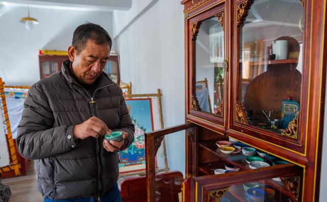 (260216) -- LHASA, Feb. 16, 2026 (Xinhua) -- Norbu Sidar checks pigment at the Xizang Academy of Thangka in Lhasa, southwest China's Xizang Autonomous Region, Feb. 10, 2026. On the afternoon of Feb. 10, sunlight streamed through the windows of the Xizang Academy of Thangka, illuminating an unfinished thangka painting. Norbu Sidar stood beside a young apprentice. He reached out, gently placing his finger on a specific spot on the canvas, and quietly guided the apprentice on the direction of the lines. 
   Thangka, renowned for its meticulous composition, vibrant colors, and profound cultural connotations, was listed among the first batch of China's national intangible cultural heritages in 2006. Recording Tibetan history, culture, medicine, astronomy, and other knowledge, it carries the spiritual beliefs and aesthetic wisdom of people in Xizang throughout the times.
   Norbu Sidar is a national-level inheritor of the Tibetan thangka. As a child, he learned thangka painting techniques from his grandfather. He recalled, "Time was most precious when I was little. I could only learn to paint thangka in my spare time after helping the family with farm and livestock work." From 2005 to 2015, he spent ten years as a restoration expert undertaking the mural restoration project at the Potala Palace. In 2016, he donated the 18 thangka works he had copied at the Potala Palace over the decade to the Palace. "These ten years have been the most meaningful part of my life," he recalled.
   In 1992, Norbu Sidar began taking on students. Ten years later, he led the founding of the Xizang Academy of Thangka. Today, as a master's supervisor at the School of Arts of Xizang University, he guides graduate students in studying the history of thangka and encourages young people to experiment with new forms of expression. To date, over 400 students are, like him, contributing to the development of Tibetan thangka art.
    After being elected as a member of the National Committee of the Chinese People's Political Consultative Conference, Norbu Sidar felt he had the responsibility to do more to make thangka, the artistic treasure in Xizang, recognized, supported and passed down through generations. (Xinhua/Tenzin Nyida)