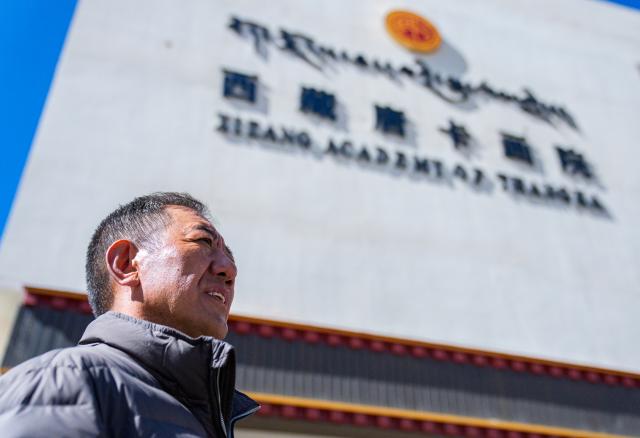 (260216) -- LHASA, Feb. 16, 2026 (Xinhua) -- Norbu Sidar stands in front of the Xizang Academy of Thangka in Lhasa, southwest China's Xizang Autonomous Region, Feb. 10, 2026. On the afternoon of Feb. 10, sunlight streamed through the windows of the Xizang Academy of Thangka, illuminating an unfinished thangka painting. Norbu Sidar stood beside a young apprentice. He reached out, gently placing his finger on a specific spot on the canvas, and quietly guided the apprentice on the direction of the lines. 
   Thangka, renowned for its meticulous composition, vibrant colors, and profound cultural connotations, was listed among the first batch of China's national intangible cultural heritages in 2006. Recording Tibetan history, culture, medicine, astronomy, and other knowledge, it carries the spiritual beliefs and aesthetic wisdom of people in Xizang throughout the times.
   Norbu Sidar is a national-level inheritor of the Tibetan thangka. As a child, he learned thangka painting techniques from his grandfather. He recalled, "Time was most precious when I was little. I could only learn to paint thangka in my spare time after helping the family with farm and livestock work." From 2005 to 2015, he spent ten years as a restoration expert undertaking the mural restoration project at the Potala Palace. In 2016, he donated the 18 thangka works he had copied at the Potala Palace over the decade to the Palace. "These ten years have been the most meaningful part of my life," he recalled.
   In 1992, Norbu Sidar began taking on students. Ten years later, he led the founding of the Xizang Academy of Thangka. Today, as a master's supervisor at the School of Arts of Xizang University, he guides graduate students in studying the history of thangka and encourages young people to experiment with new forms of expression. To date, over 400 students are, like him, contributing to the development of Tibetan thangka art.
    After being elected as a member of the National Committee of the Chinese People's Political Consultative Conference, Norbu Sidar felt he had the responsibility to do more to make thangka, the artistic treasure in Xizang, recognized, supported and passed down through generations. (Xinhua/Tenzin Nyida)