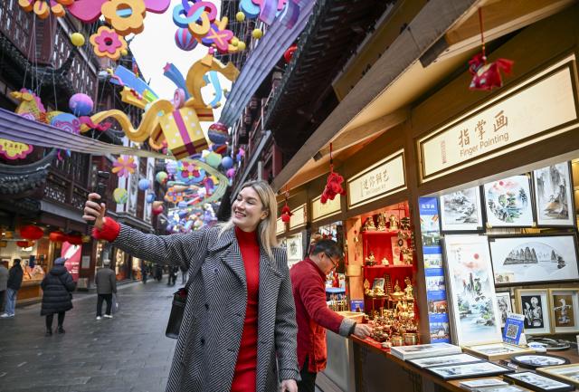 (260216) -- SHANGHAI, Feb. 16, 2026 (Xinhua) -- Aleksandra Antonenko takes short videos at a traditional crafts booth of Yuyuan Garden shopping mall in Shanghai, east China, Feb. 6, 2026.
  Aleksandra Antonenko moved from Russia to pursue her doctorate at Shanghai Jiao Tong University in 2022. She also began to show the charm of everyday life in China to the world with short video clips. 
  In the same year, she met Zhao Yiwei, now her husband, at a coffee shop. Zhao always encourages and supports her diligence, be it in academic pursue or in vlog production.
  With the Spring Festival around the corner, Aleksandra loves wandering through streets and picking out New Year goods. Back to her home, she adds her own tradition to the celebration by cooking Russian dishes for the holiday, turning the table into a blend of two cultures. 
  "The Spring Festival has deep cultural roots," Aleksandra said. "It's a time to bring family together and feel closer."
  Looking ahead, she plans to keep working toward her doctoral degree while continuing to document her life in China through videos. "Every day here brings something new," she said. "I'm excited to share real stories about China with the world."
  From a newbie international student to a Chinese daughter-in-law and a builder of cultural connections, Aleksandra's story reflects a simple belief: love knows no borders. (Xinhua/Chen Haoming)