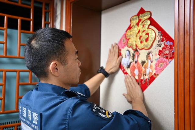 (260216) -- SOUTH CHINA SEA, Feb. 16, 2026 (Xinhua) -- Law enforcer Zhang Shengfeng posts a Spring Festival decoration featuring the Chinese character "Fu", which means good fortune, aboard the China Coast Guard (CCG) vessel Wanshan in the territorial waters of China's Huangyan Dao on Feb. 11, 2026.
  Law enforcers aboard the China Coast Guard (CCG) vessel Wanshan remain on duty during this year's Spring Festival, a most cherished moment for family reunions in China. (Photo by Zhai Yifan/Xinhua)