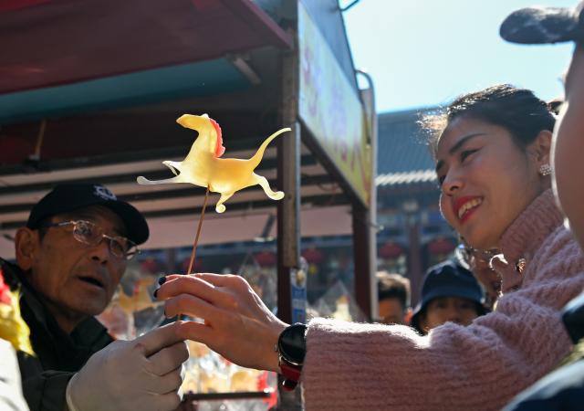 (260217) -- BEIJING, Feb. 17, 2026 (Xinhua) -- A customer holds a horse-shaped syrup figurine in north China's Tianjin, Feb. 17, 2026. This year's Spring Festival saw a surge of visitors eager to experience local cuisine, rich history and vibrant folk performances. (Xinhua/Sun Fanyue)
