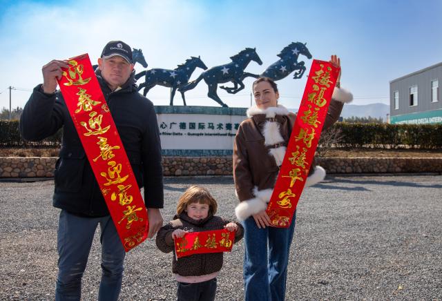 (260218) -- GUANGDE, Feb. 18, 2026 (Xinhua) -- Sasha, her husband Vasil and her daughter Maya pose for a photo with a Spring Festival couplet at the Yangtze River Delta International Equestrian Center in Dongting Town of Guangde City, east China's Anhui Province, Feb. 8, 2026. Sasha, an equestrian from Russia, once studied in Shanghai and later went to Europe to study equestrian sports, where she met coach Vasil and eventually married him. They have a lovely daughter named Maya. In 2023, Sasha's family moved to Guangde to start a new life, as her husband Vasil was invited to teach at the Yangtze River Delta International Equestrian Center.
  "Riding has always been my favorite," Sasha said in Chinese. Sasha's family now lives near the equestrian center, where she trains daily in equestrian show jumping, takes walks with her beloved horse, and sometimes helps with horse training. Looking ahead, she hopes to participate in more equestrian competitions and to one day own her own ranch.
  Beyond the racetrack, Sasha engages in cultural activities to learn about local customs and traditions. Her daughter Maya attends a local kindergarten and has learned Chinese. Her husband Vasil's equestrian teaching is well received by students. These experiences have helped Sasha feel a sense of belonging in a place once unfamiliar to her. "Guangde is picturesque and has friendly people. Living and training here makes me feel wonderful," said Sasha. (Photo by Yang Guangxue/Xinhua)