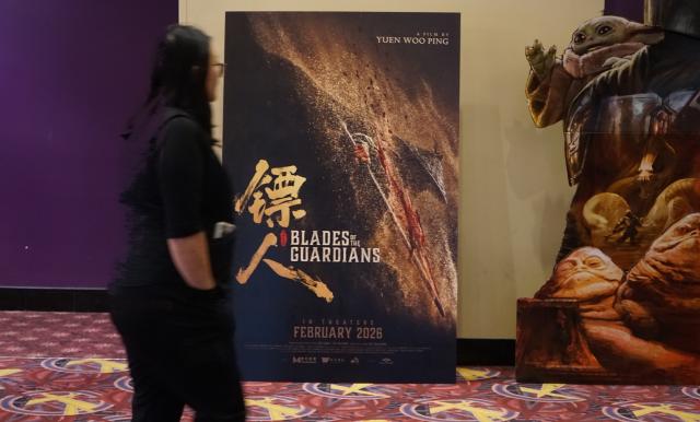 (260218) -- LOS ANGELES, Feb. 18, 2026 (Xinhua) -- A moviegoer walks past a poster of  "Blades of the Guardians," a film directed by legendary action choreographer Yuen Woo-ping, at a cinema in Monterey Park, Los Angeles County, California, the United States, Feb. 17, 2026. Multiple Chinese films are set for release in North America during the period of Chinese New Year, also known as the Spring Festival, including two highly-anticipated blockbusters premiering Tuesday, the Chinese Lunar New Year's Day.
   TO GO WITH "Multiple Chinese blockbusters to hit North American screen during Chinese New Year" (Photo by Zeng Hui/Xinhua)