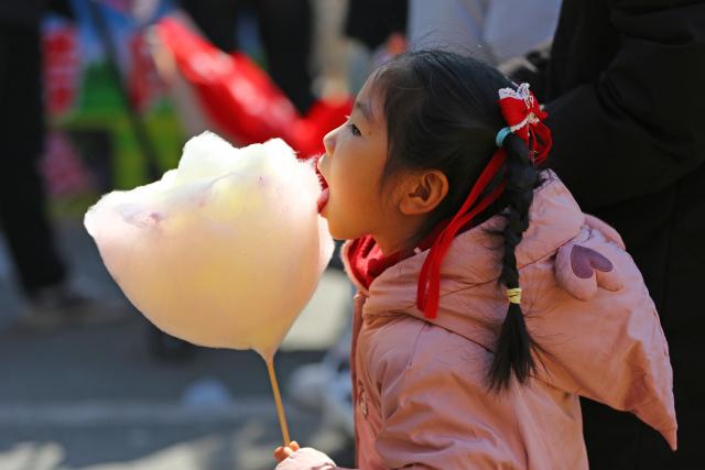 (260218) -- BEIJING, Feb. 18, 2026 (Xinhua) -- A girl tastes cotton candy at a park in Tengzhou, east China's Shandong Province, Feb. 17, 2026. During this Spring Festival holiday, traditional Chinese New Year food and trendy cuisines have altogether become highlights for peoples' holiday consumption. (Photo by Li Zhijun/Xinhua)