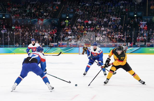 (260218) -- MILAN, Feb. 18, 2026 (Xinhua) -- John Peterka (1st R) of Germany shoots during the ice hockey men's play-offs quarterfinal between the Slovakia and Germany at the Milan-Cortina 2026 Olympic Winter Games in Milan, Italy, Feb. 18, 2026. (Xinhua/Wang Kaiyan)