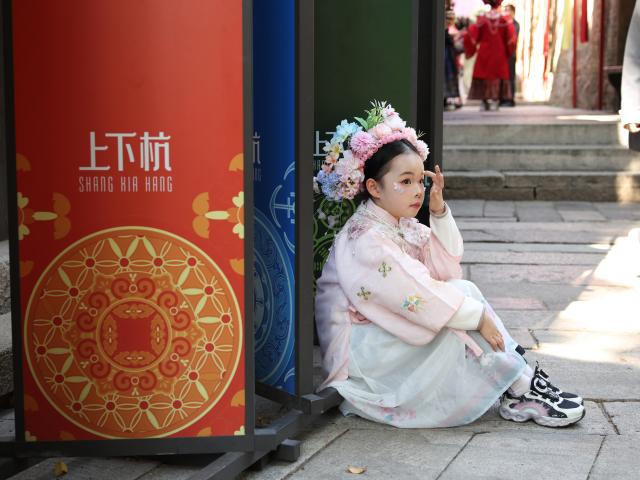(260222) -- FUZHOU, Feb. 22, 2026 (Xinhua) -- A girl in traditional costumes rests at the Shangxiahang traditional block in Fuzhou, southeast China's Fujian Province, Feb. 21, 2026. People wearing traditional costumes enlightened historic blocks in Fuzhou during the Spring Festival holiday. (Xinhua/Jiang Kehong)