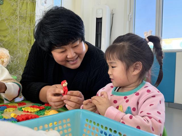 (260222) -- QINGDAO, Feb. 22, 2026 (Xinhua) -- Zhu Xiuqin plays with a child at the Kangbei Childcare Center in Lyujia Village of Cuijiaji Town, Qingdao, east China's Shandong Province, Dec. 30, 2025. TO GO WITH "China Focus: Cradle next to a greenhouse: China brings daycare to the fields" (Xinhua/Zhang Liyuan)