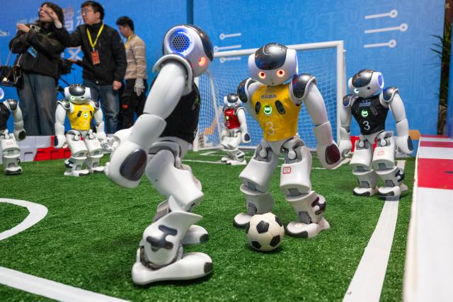 (260224) -- WUHAN, Feb. 24, 2026 (Xinhua) -- Humanoid robots play football in Wuhan, central China's Hubei Province, Feb. 24, 2026. A variety of electric vertical takeoff and landing (eVTOL) aircraft and humanoid robots made their debut at an event in Wuhan, showcasing the province's latest achievements of industries such as low-altitude economy and artificial intelligence. (Xinhua/Xiao Yijiu)