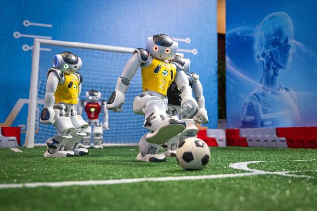 (260224) -- WUHAN, Feb. 24, 2026 (Xinhua) -- Humanoid robots play football in Wuhan, central China's Hubei Province, Feb. 24, 2026. A variety of electric vertical takeoff and landing (eVTOL) aircraft and humanoid robots made their debut at an event in Wuhan, showcasing the province's latest achievements of industries such as low-altitude economy and artificial intelligence. (Xinhua/Xiao Yijiu)