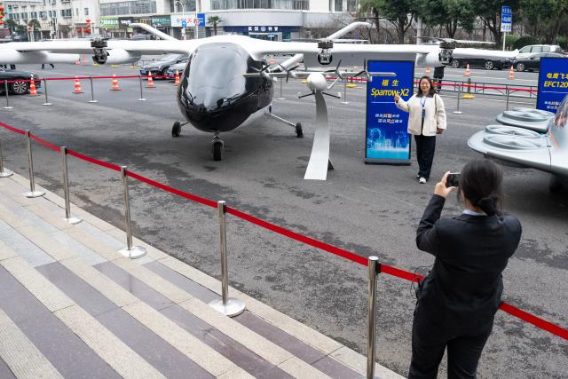 (260224) -- WUHAN, Feb. 24, 2026 (Xinhua) -- A visitor poses for photos with an electric vertical takeoff and landing (eVTOL) aircraft in Wuhan, central China's Hubei Province, Feb. 24, 2026. A variety of electric vertical takeoff and landing (eVTOL) aircraft and humanoid robots made their debut at an event in Wuhan, showcasing the province's latest achievements of industries such as low-altitude economy and artificial intelligence. (Xinhua/Xiao Yijiu)