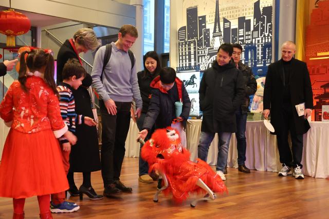 (260224) -- PARIS, Feb. 24, 2026 (Xinhua) -- People interact with a robotic dog dressed in a red lion dance costume during a Chinese New Year event at the China Cultural Center in Paris, France, on Feb. 14, 2026. TO GO WITH "Roundup: Future-oriented Chinese New Year in France blends tradition, technology" (Xinhua/Zhang Baihui)