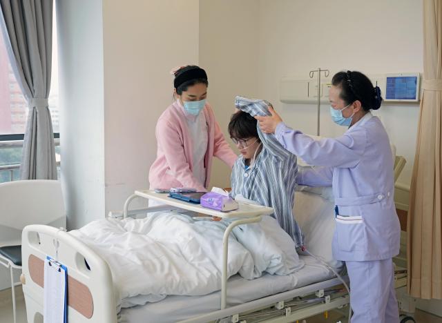 (260227) -- SHANGHAI, Feb. 27, 2026 (Xinhua) -- A nurse (L) and nursing assistant (R) help an inpatient with post-surgery rehabilitation exercises at a hospital in Shanghai, east China, Feb. 26, 2026. China's hospitals are piloting "companion-free" care services to ease the heavy burden of daily care-giving on the inpatients' families.
  The new mode of operation requires hosting hospitals to directly employ trained nursing assistants to provide 24-hour non-medical care for inpatients with particular needs. 
   Such services used to rely solely on family members of the inpatients or private caregivers they hire. (Xinhua/Liu Ying)