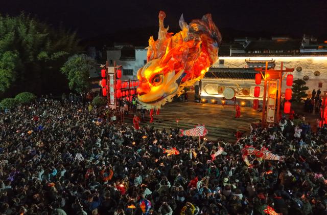 (260228) -- HUANGSHAN, Feb. 28, 2026 (Xinhua) -- An aerial drone photo taken on Feb. 27, 2026 shows people watching an Ao Fish lantern parade at the Tangmo ancient town in Huangshan City, east China's Anhui Province. The lantern parade was held here in celebration of the upcoming Lantern Festival on Friday, featuring the Ao Fish, a mythical Chinese creature with a dragon's head and a fish's body. (Photo by Shi Yalei/Xinhua)