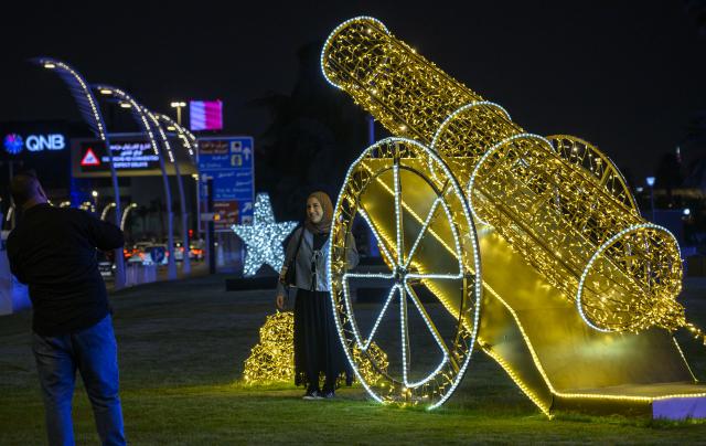 (260228) -- DOHA, Feb. 28, 2026 (Xinhua) -- A visitor poses for photos with an illuminated decorative cannon installation during the holy month of Ramadan in Doha, Qatar, Feb. 27, 2026. (Photo by Nikku/Xinhua)