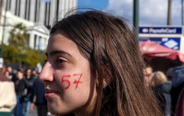 (260301) -- ATHENS, March 1, 2026 (Xinhua) -- A young woman with the number "57" painted on her cheek stands among demonstrators at Syntagma Square in Athens, Greece, Feb. 28, 2026. Thousands of people took part in dozens of demonstrations across Greece on Saturday to mark the third anniversary of the train collision in Tempi, central Greece, which claimed 57 lives. (Xinhua/Marios Lolos)