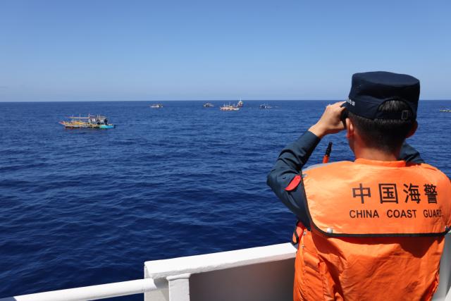 (260301) -- SOUTH CHINA SEA, March 1, 2026 (Xinhua) -- A law enforcer of China Coast Guard (CCG) vessel Wanshan observes Philippine vessels in waters off China's Huangyan Dao in the South China Sea, Feb. 27, 2026. The CCG on Friday drove away Philippine vessels that illegally intruded into China's territorial waters off Huangyan Dao in the South China Sea. (CCG/Handout via Xinhua)