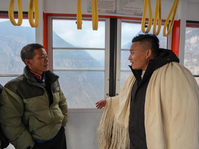 (260302) -- HANYUAN, March 2, 2026 (Xinhua) -- Zheng Wangchun (R) talks with a migrant worker returning home inside a cable car in Gulu Village of Hanyuan County, southwest China's Sichuan Province, Jan. 28, 2026.
  Perched on a cliff at the entrance to the Dadu River Grand Canyon, Gulu Village in Sichuan Province was long isolated by poor transportation. The opening of a cableway in 2018 marked a turning point, cutting the journey from three to four hours down to just three to five minutes. 
  Zheng Wangchun is the head of the village committee and secretary of the Party committee of Gulu Village, and a deputy to the National People's Congress (NPC). Over the past years, Zheng has led villagers in developing a new path of integrated agricultural, cultural and tourism development, breathing new life into this Yi ethnic village. Villagers have opened homestays for visitors, and multiple scenic photo spots to enhance the visitor experience. At the same time, the village has expanded characteristic industries such as walnuts, Sichuan pepper, and goat farming. 
  Since taking office, Zheng has submitted suggestions including expanding internet access in rural areas and strengthening wildlife protection while minimizing its impact on farmers' livelihoods. "The smiles of villagers are the most valuable rewards for grassroots work," Zheng said. (Xinhua/Wang Xi)