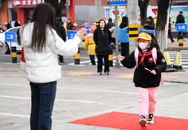 (260302) -- BEIJING, March 2, 2026 (Xinhua) -- A teacher welcomes students in front of a primary school in Pinggu District of Beijing, capital of China, March 2, 2026. A new semester kicked off for primary and secondary schools in many parts of China on Monday. (Xinhua/Ren Chao)