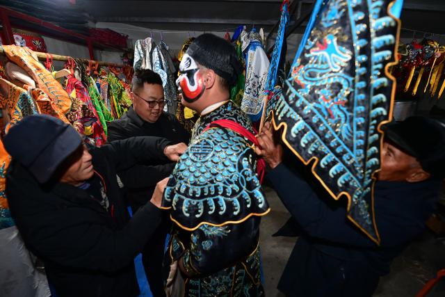 (260302) -- BAOJI, March 2, 2026 (Xinhua) -- Villagers help a member of a Shehuo parade team put on performance costumes in Huanghuayu Village in Longxian County of Baoji City, northwest China's Shaanxi Province, in the early morning of March 2, 2026.
  Shehuo is a type of traditional Chinese folk art form. Longxian County held a special local Shehuo parade on Monday, which features performers on horseback adorned with simple yet exquisite facial make-up.
  The Shehuo parade is a long-standing and widely popular performance in rural China. It originated in ancient sacrificial ceremonies held to pray for good harvests about 2,000 years ago.
  Over time, as dance and song performances were incorporated, it gradually evolved into a folk custom staged during the Spring Festival and Lantern Festival, believed to ward off bad luck and usher in a fresh start for the new year.
  The Shehuo folk performance in Baoji was added to China's national intangible cultural heritage list in 2006. In recent years, the local Shehuo tradition in Longxian County has continued to thrive through ongoing inheritance and innovation. (Xinhua/Zou Jingyi)