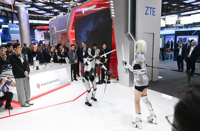 (260302) -- BARCELONA, March 2, 2026 (Xinhua) -- People watch a performance by a robot and a woman at the booth of ZTE during the 2026 Mobile World Congress (MWC) in Barcelona, Spain, March 2, 2026. The 2026 MWC opened on Monday in Barcelona, Spain, under the theme "The IQ Era," with a focus on intelligent infrastructure, AI connectivity and integration, enterprise-level AI applications, AI ecosystem collaboration, inclusive technology and innovation-driven transformation. (Xinhua/Cheng Min)