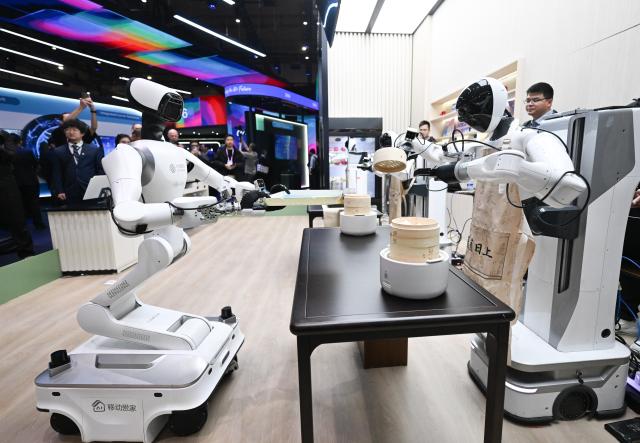 (260302) -- BARCELONA, March 2, 2026 (Xinhua) -- People view robots displayed at the booth of China Mobile during the 2026 Mobile World Congress (MWC) in Barcelona, Spain, March 2, 2026. The 2026 MWC opened on Monday in Barcelona, Spain, under the theme "The IQ Era," with a focus on intelligent infrastructure, AI connectivity and integration, enterprise-level AI applications, AI ecosystem collaboration, inclusive technology and innovation-driven transformation. (Xinhua/Cheng Min)