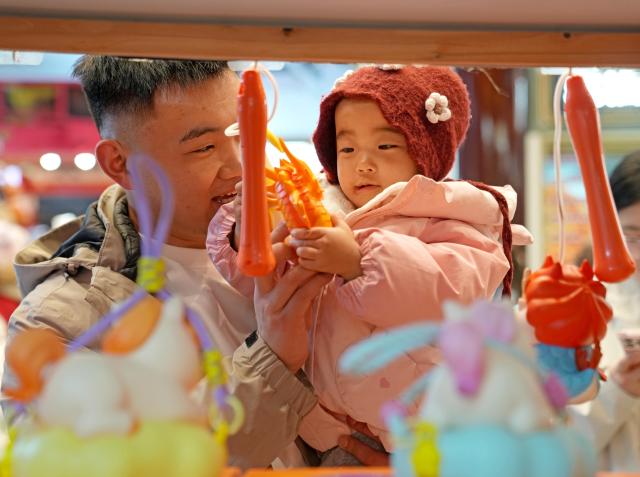 (260303) -- SHANGHAI, March 3, 2026 (Xinhua) -- A tourist and a child select lanterns during the Lantern Festival celebrations at the Yuyuan Garden in Shanghai, east China, March 2, 2026. Various activities were held during this year's Lantern Festival celebrations at Yuyuan Garden of east China's Shanghai, drawing large numbers of tourists. (Xinhua/Liu Ying)