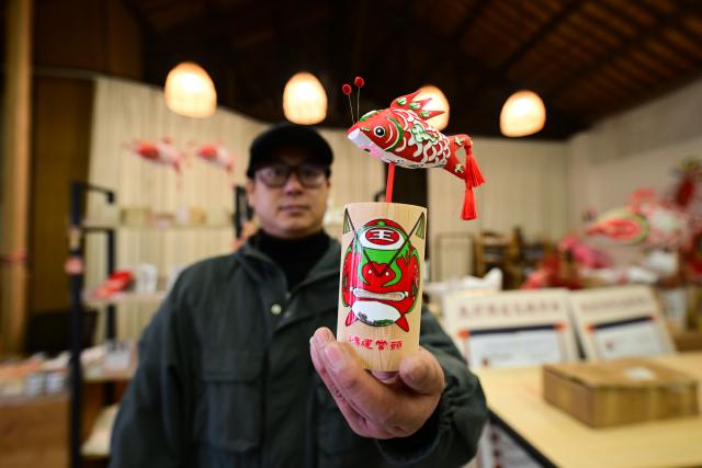 (260303) -- SHEXIAN, March 3, 2026 (Xinhua) -- A staff member presents a product at a souvenir shop themed on fish-shaped lanterns in Zhanqi Village, Shexian County, Huangshan City of east China's Anhui Province, Jan. 29, 2026.
  Local villagers in Shexian have the tradition to make fish-shaped lanterns, an intangible cultural heritage, on festival days to pray for harvest and good fortune. 
   The parade with fish-shaped lanterns is an important folk cultural activity held during traditional festivals.
   Nowadays, apart from parades with fish-shaped lanterns, local people have made efforts on developing new business forms related to the fish-shaped lantern including tourism and cultural and creative products. (Xinhua/Zhou Mu)