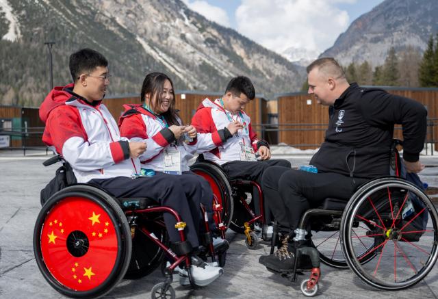 (260303) -- CORTINA D'AMPEZZO, March 3, 2026 (Xinhua) -- Athletes exchange pins at the Paralympic Village of the Milan-Cortina 2026 Paralympic Winter Games in Cortina d'Ampezzo, Italy, March 3, 2026. (Xinhua/Lian Zhen)