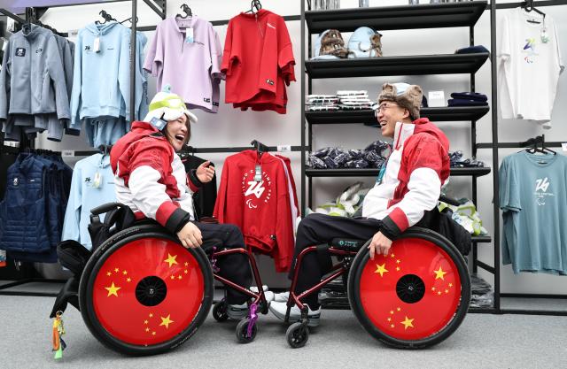 (260303) -- CORTINA D'AMPEZZO, March 3, 2026 (Xinhua) -- Chen Jianxin (R) and Li Nana of China select souvenir in the official store at the Paralympic Village of the Milan-Cortina 2026 Paralympic Winter Games in Cortina d'Ampezzo, Italy, March 3, 2026. (Xinhua/Wang Kaiyan)