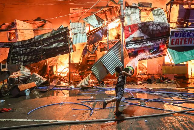 (260307) -- Beijing, March 7, 2026 (Xinhua) -- A resident throws a bucket of water to put out a huge fire engulfing shanties at a slum area in Quezon City, the Philippines, on March 6, 2026. (Xinhua/Rouelle Umali)