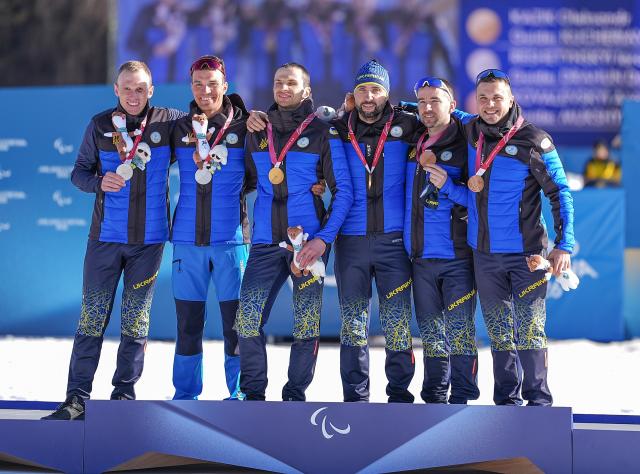 (260308) -- TESERO, March 8, 2026 (Xinhua) -- Gold medalist Oleksandr Kazik (3rd L) of Ukraine and guide Serhii Kucheriavyi (3rd R) celebrate on the podium alongside silver medalist Iaroslav Reshetynskyi (1st L) of Ukraine and guide Dmytro Drahun (2nd L) and bronze medalist Anatolii Kovalevskyi (2nd R) of Ukraine and guide Oleksandr Mukshyn during the awarding ceremony for the para biathlon men's sprint Vision Impaired at the Milan-Cortina 2026 Paralympic Winter Games in Tesero, Italy, March 7, 2026. (Xinhua/Hou Zhaokang)