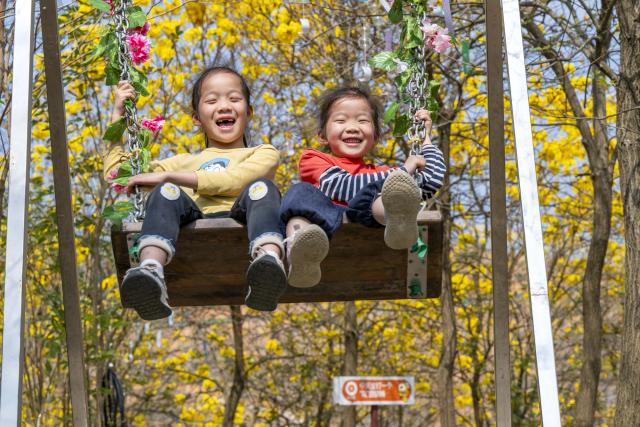 (260308) -- BEIJING, March 8, 2026 (Xinhua) -- Children play on a swing under blooming flowers in Wuzhou, south China's Guangxi Zhuang Autonomous Region, March 7, 2026. (Photo by He Huawen/Xinhua)
