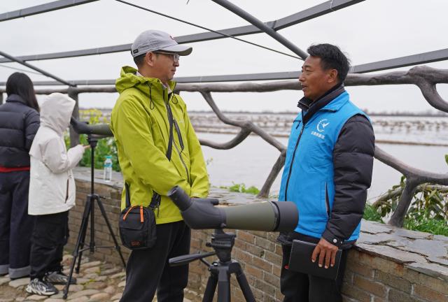 (260310) -- YUGAN, March 10, 2026 (Xinhua) -- Jiang Liangqing shares migratory birds conservation knowledge with a tourist in Yugan County, east China's Jiangxi Province, on Feb. 27, 2026. Poyang Lake, China's largest freshwater lake and an extensive wetland, is a vital wintering and stopover site along the East Asian-Australasian Flyway. Every winter, thousands of Siberian cranes, a critically endangered species, gather in Yugan County, which lies to the southeast of the lake. 
   Decades ago, local villagers faced a dilemma. On the one hand, capturing or killing migratory birds was against the law. On the other hand, leaving the birds undisturbed could lead to serious crop losses. To reduce the damage, villagers around the lake often went to great lengths to drive birds away, using firecrackers, beating gongs, and setting up scarecrows.
   To address the problem, local authorities introduced a compensation mechanism. Villagers whose crops have been damaged in the course of wetland and migratory bird conservation can receive compensation. The policy has helped reduce crop losses for villagers while supporting bird conservation. As a result, more migratory birds now winter at Poyang Lake, and the local birdwatching economy has flourished.
   Jiang Liangqing, once troubled by the "bird dilemma," is now a bird guardian in Yugan County. "I have more than 100 mu (about 6.67 hectares) of rice fields, where migratory birds often come to forage," Jiang said. "It used to be a problem, but now I receive compensation after local authorities assess my crop losses."
   "Now I'm a bird guardian. I patrol the wetlands every day and share knowledge about bird conservation with tourists," Jiang said. Like him, many local villagers have joined conservation efforts, including raising ecological awareness and patrolling wetlands. (Xinhua/Wan Xiang)