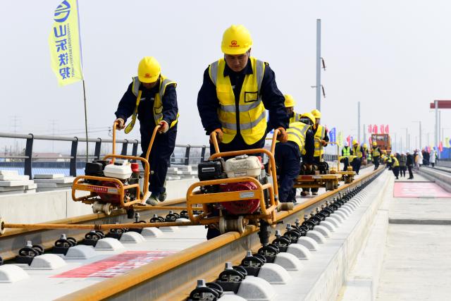 (260310) -- BINZHOU, March 10, 2026 (Xinhua) -- Staff members lay tracks at Binzhou railway station of the Jinan-Binzhou high-speed railway in Binzhou City, east China's Shandong Province, on March 10, 2026. The high-speed railway, which links the province's cities of Jinan and Binzhou and with a designed speed of 350 km/h, has officially entered the full-line track-laying operation phase on Tuesday. (Xinhua/Guo Xulei)