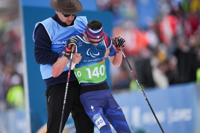 (260311) -- TESERO, March 11, 2026 (Xinhua) -- Karl Tabouret (R) of France is helped up after winning the final match of the men's 10km interval start classic standing of Para Cross-Country Skiing at the Milan-Cortina 2026 Paralympic Winter Games in Tesero, Italy, March 11, 2026. (Xinhua/Lian Zhen)