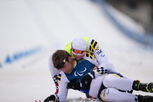 (260311) -- TESERO, March 11, 2026 (Xinhua) -- Zebastian Modin (Bottom) of Sweden is helped up by his guider Emli Talsi after the men's 10km interval start classic Vision Impaired of Para Cross-Country Skiing at the Milan-Cortina 2026 Paralympic Winter Games in Tesero, Italy, March 11, 2026. (Xinhua/Lian Zhen)