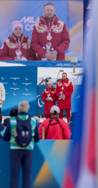 (260311) -- TESERO, March 11, 2026 (Xinhua) -- Anastasiia Bagiian (L) of Russia and her guider Sergei Siniakin stand on the podium during the awarding ceremony of the women's 10km interval start classic Vision Impaired of Para Cross-Country Skiing at the Milan-Cortina 2026 Paralympic Winter Games in Tesero, Italy, March 11, 2026. (Xinhua/Lian Zhen)
