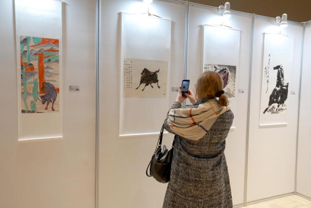 (260311) -- BISHKEK, March 11, 2026 (Xinhua) -- A visitor takes photos of exhibits at a Chinese painting exhibition on the theme of "horse" in Bishkek, Kyrgyzstan, on March 10, 2026. The exhibition opened here on Tuesday, showcasing about 50 works on horses in different styles by renowned Chinese painters. (Photo by Roman/Xinhua)