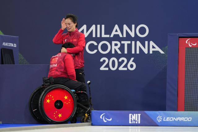 (260312) -- CORTINA D'AMPEZZO, March 12, 2026 (Xinhua) -- Coach Ru Xia (R) of China sheds tears and hugs Wang Meng after winning the wheelchair curling mixed doubles gold medal game between China and South Korea at the Milan-Cortina 2026 Paralympic Winter Games in Cortina D'ampezzo, Italy, March 11, 2026. (Xinhua/Lian Yi)