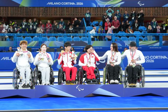 (260312) -- CORTINA D'AMPEZZO, March 12, 2026 (Xinhua) -- Gold medalists Yang Jinqiao (3rd L)/Wang Meng (3rd R) of China, silver medalists Lee Yongsuk (1st L)/Baek Hyejin (2nd L) of South Korea, and bronze medalists Polina Rozkova (2nd R)/Agris Lasmans of Latvia attend the awarding ceremony for the wheelchair curling mixed doubles event at the Milan-Cortina 2026 Paralympic Winter Games in Cortina D'ampezzo, Italy, March 11, 2026. (Xinhua/Lian Yi)