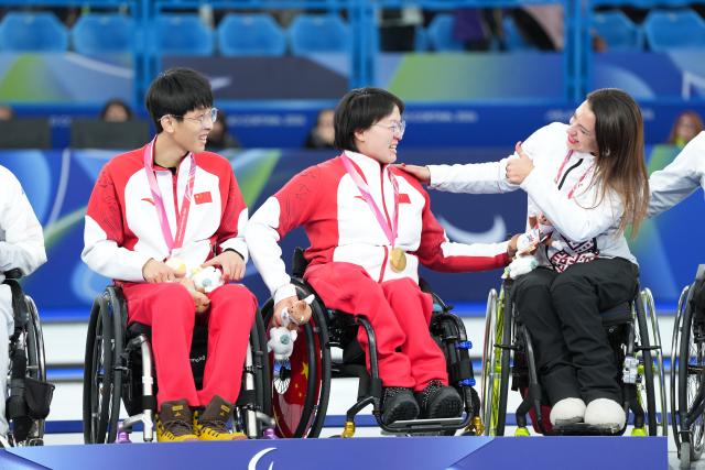 (260312) -- CORTINA D'AMPEZZO, March 12, 2026 (Xinhua) -- Bronze medalist Polina Rozkova (1st R) of Latvia gives a thumbs-up to Yang Jinqiao (1st L) /Wang Meng (2nd L) of China during the awarding ceremony for the wheelchair curling mixed doubles event at the Milan-Cortina 2026 Paralympic Winter Games in Cortina D'ampezzo, Italy, March 11, 2026. (Xinhua/Lian Yi)