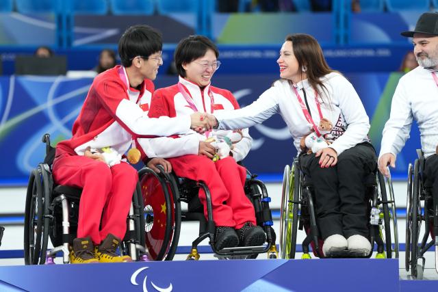 (260312) -- CORTINA D'AMPEZZO, March 12, 2026 (Xinhua) -- Bronze medalist Polina Rozkova (2nd R) of Latvia shakes hands with Yang Jinqiao (1st L) /Wang Meng (2nd L) of China during the awarding ceremony for the wheelchair curling mixed doubles event at the Milan-Cortina 2026 Paralympic Winter Games in Cortina D'ampezzo, Italy, March 11, 2026. (Xinhua/Lian Yi)