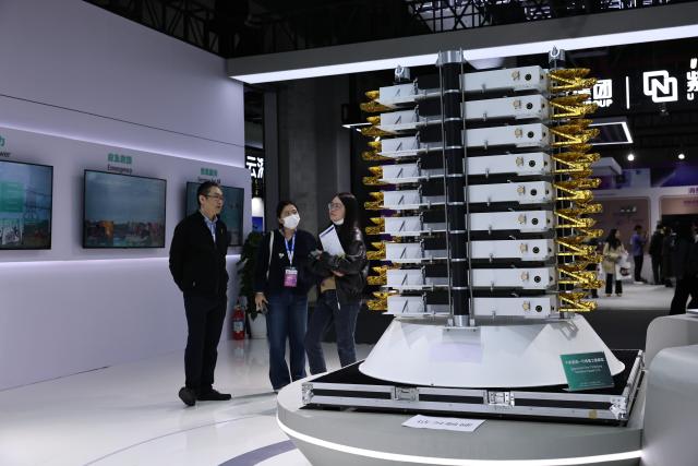 (260312) -- SHANGHAI, March 12, 2026 (Xinhua) -- Visitors are pictured beside a model of stacked satellites during the 2026 Appliance & Electronics World Expo (AWE2026) in east China's Shanghai, March 12, 2026. The AWE2026 kicked off in Shanghai on Thursday. More than 1,200 enterprises from all over the world gathered at the expo to showcase their latest innovations. (Xinhua/Fang Zhe)