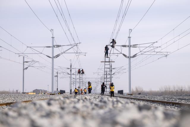 (260313) -- HARBIN, March 13, 2026 (Xinhua) -- Workers install catenary systems at the construction site of Suihua South Station of the Harbin-Yichun high-speed railway in Suihua, northeast China's Heilongjiang Province, March 13, 2026. Workers from China Railway Wuhan Electrification Bureau Group are pressing ahead with the construction of the communication, signaling and power supply systems for the 318-kilometer Harbin-Yichun high-speed railway. At present, 90% of the project has been completed. (Xinhua/Zhang Tao)